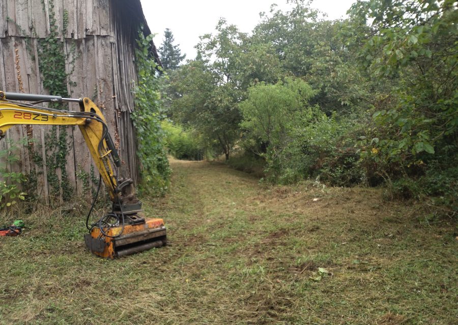 Chemin de parcelle rouvert au broyeur monté sur mini-pelle, le long d'une grange en bois